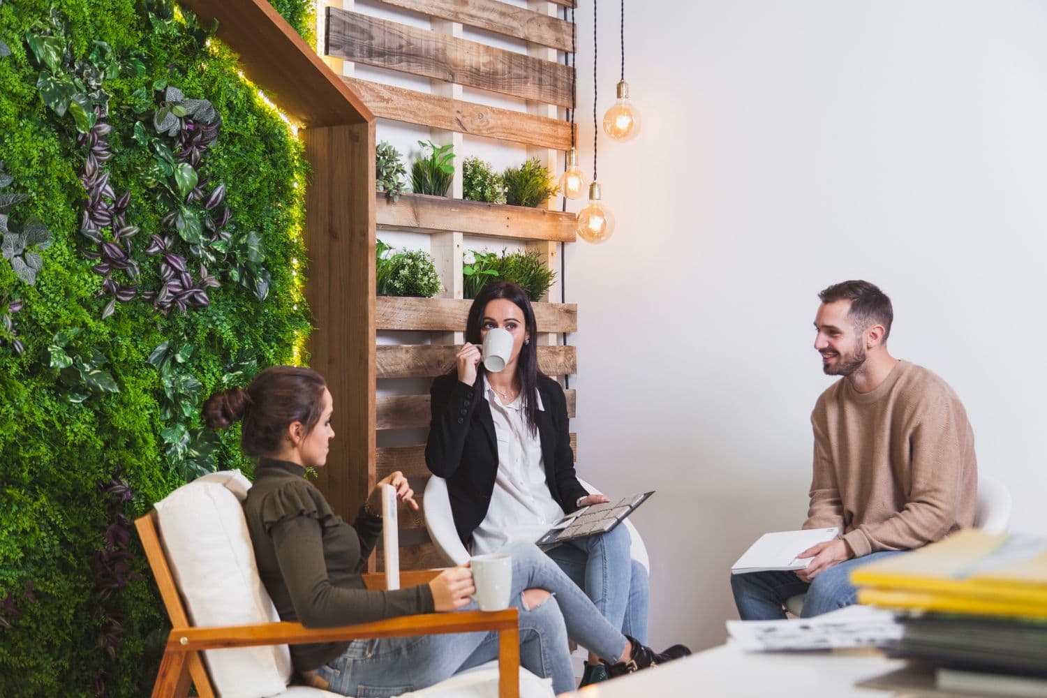 Kantoor met groene moswand en houten muur met planten erin. Drie mensen zitten ervoor. 