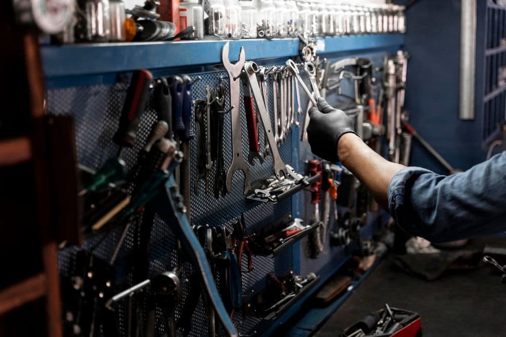 Een hand pakt gereedschap van een gereedschapswand af. De hand is in een latex handschoen gestoken. 